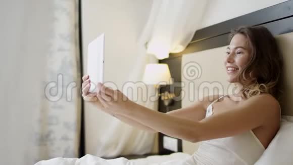 躺在床上的微笑女人正在平板电脑上视频聊天视频的预览图