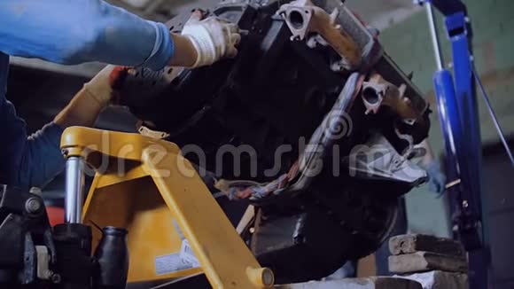 两名机械师在起重机的帮助下将汽车发动机装载到手推车上以便进一步运输视频的预览图