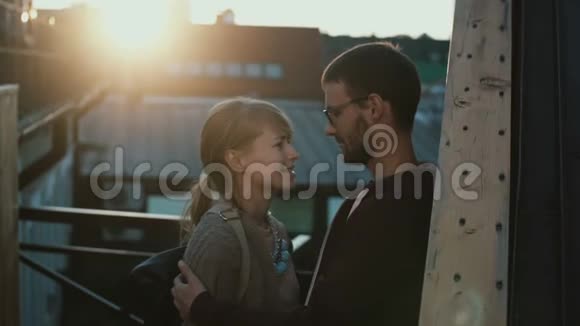 年轻迷人的夫妇站在阳台上在日落时交谈女人笑着拥抱男人视频的预览图