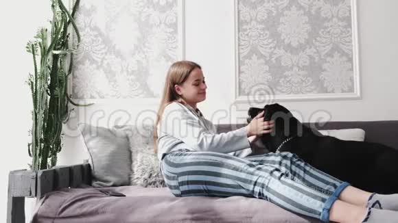 布吕内特女孩穿着休闲服装在白色房间里抚摸黑色拉布拉多坐在沙发上视频的预览图