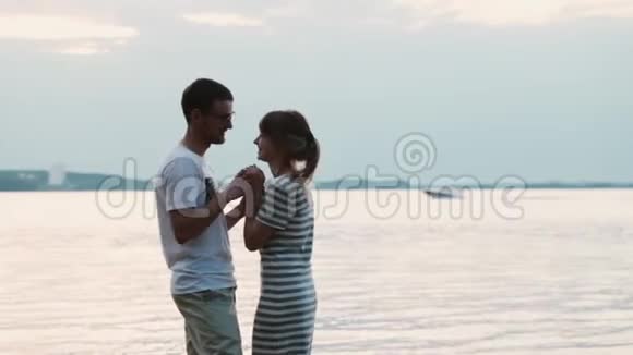 美丽的年轻夫妇站在海滩上接吻迷人的男人和女人拥抱在河岸上视频的预览图