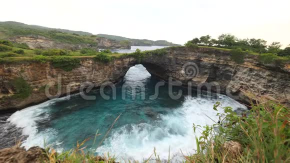 惊人的自然岩石拱门在美丽的破碎海滩在努沙佩尼达岛印度尼西亚4K大众旅游景点视频的预览图