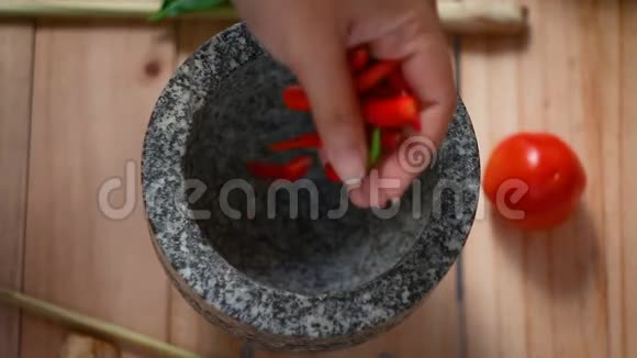 女式手用灰泥打红热鲜辣椒蒜末烹饪前准备拌料视频的预览图