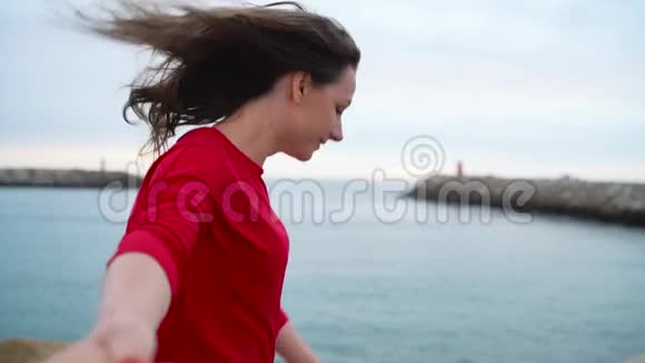 跟着我快乐的年轻女子穿着红色的连衣裙拉着男人手牵手走到海滩上的灯塔视频的预览图