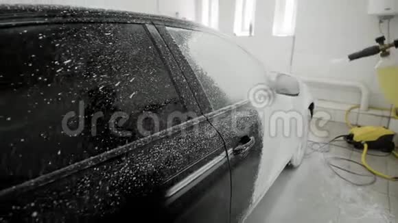 工人用肥皂泡沫覆盖汽车车身以便在车库里清洗用软管喷洒洗车视频的预览图