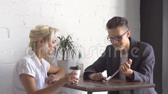 男人和女人坐在咖啡馆的桌子旁他们聊天看平板电脑视频的预览图