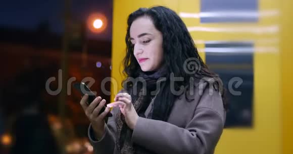 美丽快乐的年轻漂亮女人穿着棕色外套带着深蓝色围巾和长长的深色头发享受咖啡信息视频的预览图