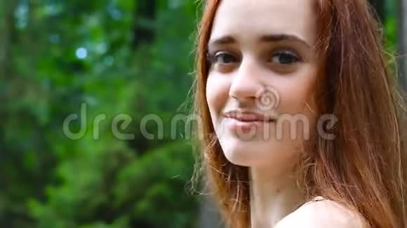 微笑的年轻女子特写的肖像与夏日公园的绿色映衬视频的预览图