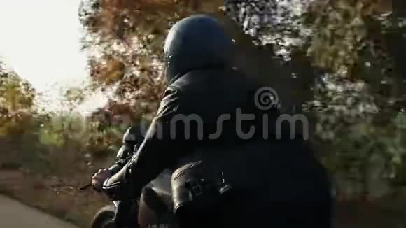 秋天阳光明媚的一天一个穿着黑色头盔和皮夹克的男人骑着摩托车在沥青路上树木视频的预览图