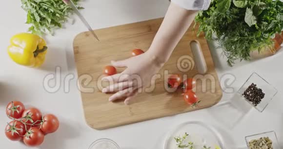 女人把红樱桃西红柿切成两半用刀切在白色厨房的木板上准备沙拉视频的预览图