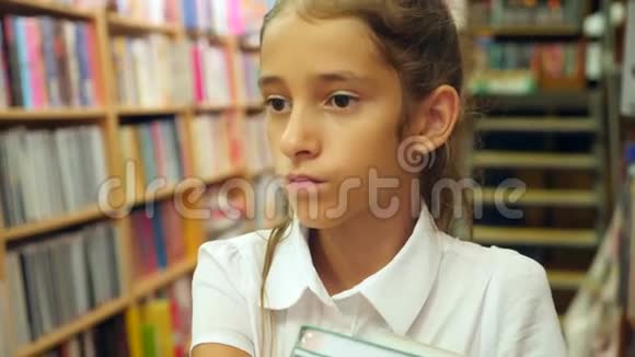 一幅812岁女孩站在图书馆的肖像背景中书架的书架4k慢视频的预览图
