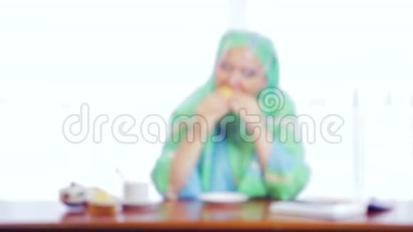 一个穿着浅绿色围巾的年轻穆斯林女人在咖啡馆里吃汉堡视频的预览图