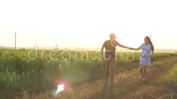 年轻的男人和女人牵着手带着野花穿过一片田野慢动作视频的预览图