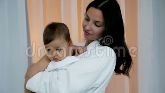 一个穿着白色浴袍抱着儿子的女人视频的预览图