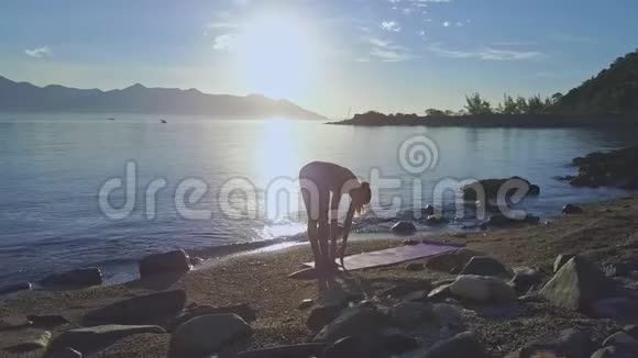 在海洋上空的太阳下在瑜伽姿势中Drone旋转着女孩视频的预览图