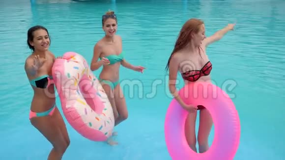 最好的朋友穿着泳衣带着蓝色的水在游泳池里跳舞夏天快乐的女孩带着粉红色的充气戒指视频的预览图