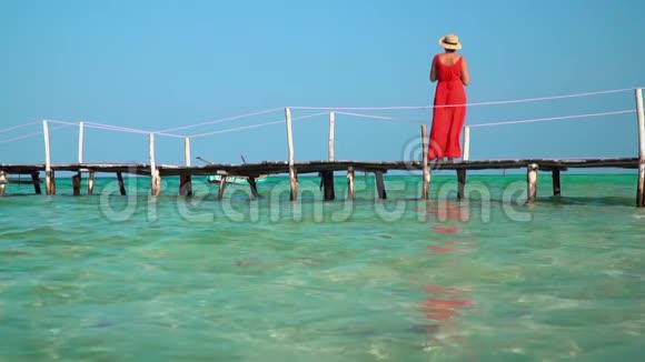 穿着红色长裙的女人这位穿红色衣服的年轻女子在码头上花钱远远地看着岛上阳光明媚的一天视频的预览图