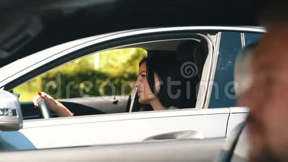 年轻的黑发女人在车里和邻车里的男人说话视频的预览图