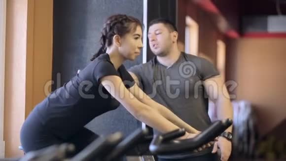 私人教练看着一个女人在固定的自行车上做负载视频的预览图
