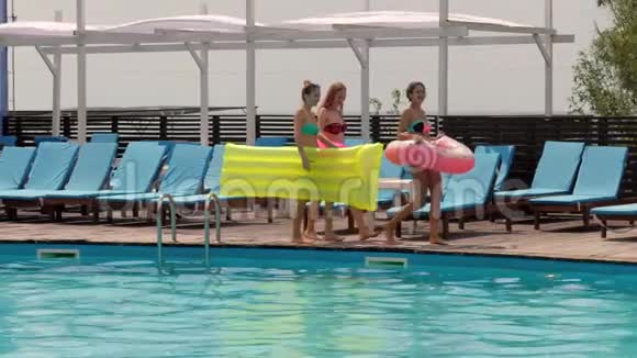 穿着泳衣的女朋友从木墩上跳进了带蓝色水的游泳池女孩们在泳池边休息视频的预览图