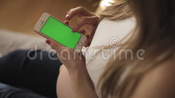 孕妇坐在沙发上用智能手机加绿色屏幕视频的预览图
