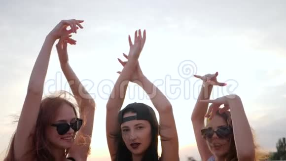 闭着脸的女朋友夏天的傍晚快乐的好朋友在海滩上夕阳下跳舞三个女人举起手臂视频的预览图
