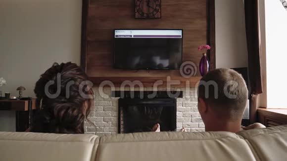 恋爱中的年轻夫妇正躺在沙发上看电视视频的预览图