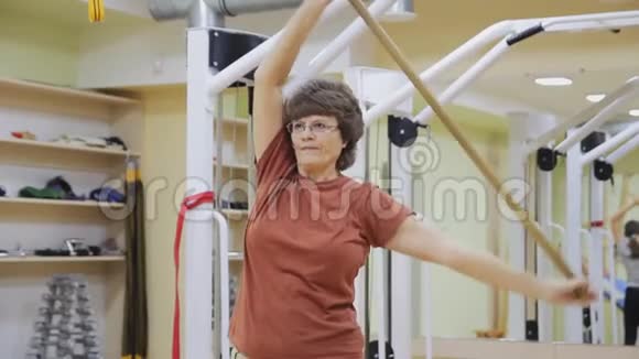老年妇女伸展身体在健身室用棍子做倾斜运动健康体操活跃的老年人视频的预览图