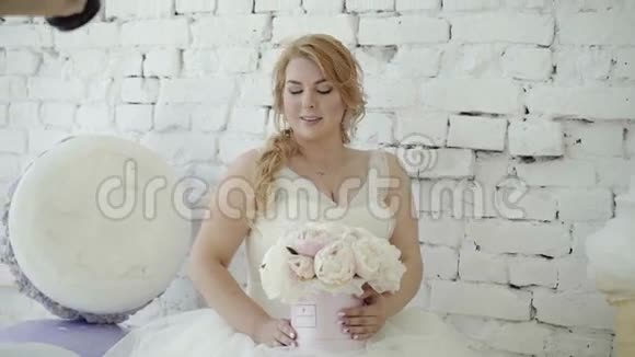 可爱的年轻金发女郎穿着婚纱花束在背景巨大的冰块上为摄影师摆姿势视频的预览图