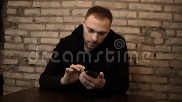 年轻的美女坐在砖墙附近的咖啡馆里用智能手机独自上网视频的预览图