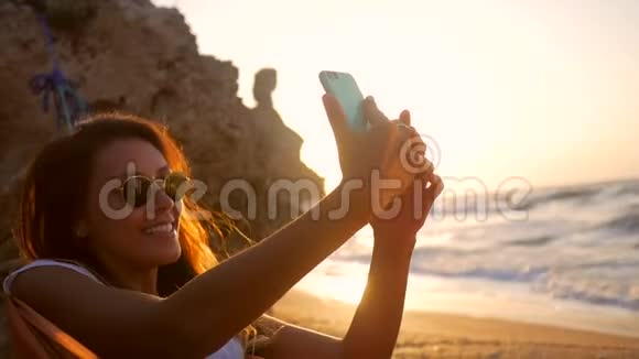 年轻的混合种族女孩拍摄自拍照片同时放松在海滩上的吊床在惊人的日落高清慢速运动视频的预览图