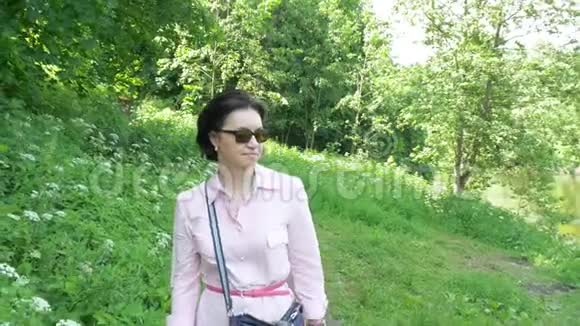 一个戴着太阳镜的中年妇女在公园里慢慢地走着视频的预览图