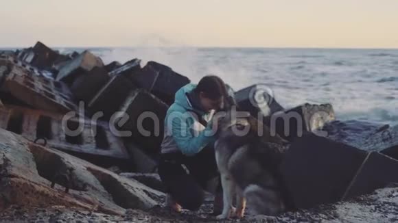 日落时分年轻美丽的女性和西伯利亚哈士奇狗在海滩上散步动作缓慢视频的预览图