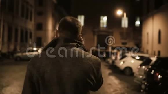 晚上年轻英俊的男人走在街上用智能手机与朋友交谈视频的预览图