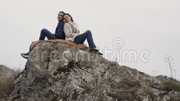 在刮风的日子里可爱的夫妇拥抱在岩石的顶部4K视频的预览图