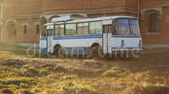 旧的老式白色蓝色苏联旧公共汽车在阳光明媚的夏日在黄橙色砖墙前的田野视频的预览图
