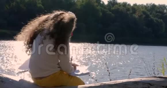 美丽快乐时尚欢乐欧洲可爱的小女孩坐在河边画在桌子上4K视频的预览图