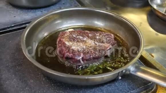 一大块牛排是在煎锅里炒的里面放着香料在餐厅的厨房里放着一根百里香枝准备美食视频的预览图