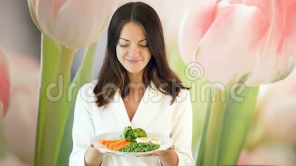 穿着白色长袍的漂亮女孩拿着一大盘煮熟的蔬菜向前推健康和适当营养视频的预览图