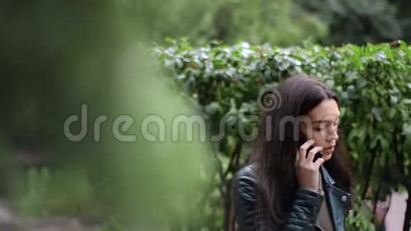 美丽的黑发女郎在公园的树间散步打电话视频的预览图
