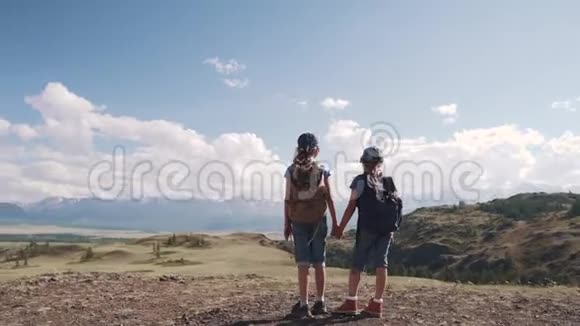 旅行者的孩子们欣赏雪峰的迷人景色两个小女孩背着背包在山上视频的预览图