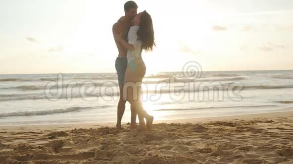 快乐的一对夫妻在日落时在海边亲吻和拥抱年轻人和女人相爱在一起玩视频的预览图