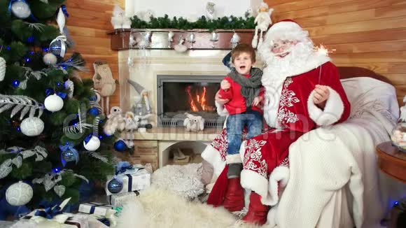 小男孩坐在圣诞老人腿上手里拿着火花孩子和快乐的圣尼古拉斯庆祝圣诞节视频的预览图