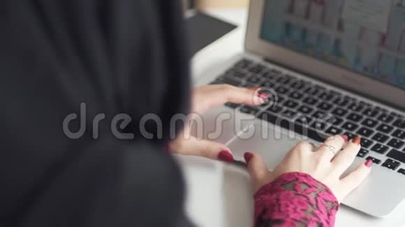 无法辨认的穆斯林妇女戴着头巾在咖啡馆里用现代笔记本电脑工作看她的手学习或工作视频的预览图