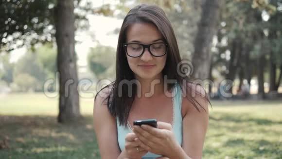 利用电话网上购物理念特写公园草坪上年轻美女的肖像视频的预览图