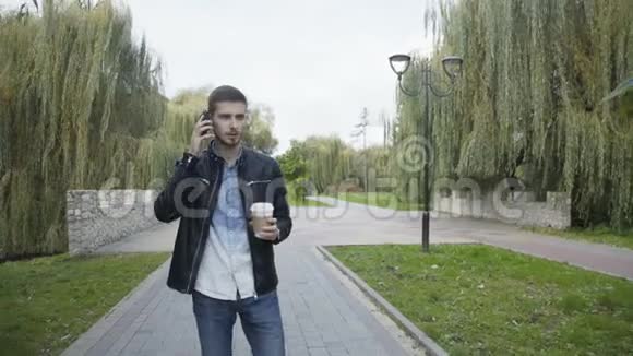 4K公园的一个手拿咖啡的年轻人在打电话视频的预览图