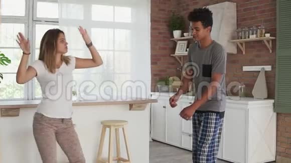早上在家快乐的年轻夫妇穿着睡衣在厨房里跳舞听音乐一对夫妇视频的预览图
