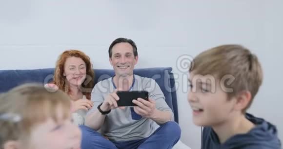 父母拍摄孩子一起玩的视频坐在卧室的床上幸福的家庭一起度过时光视频的预览图