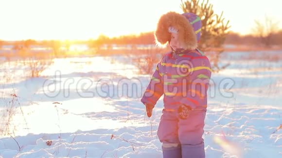 这个孩子在冬天在日落的背景下穿过雪堆视频的预览图