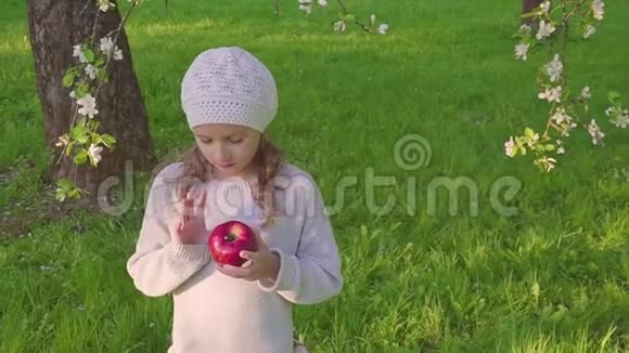 小女孩肖像吃红苹果户外花圃背景上有苹果的女孩视频的预览图